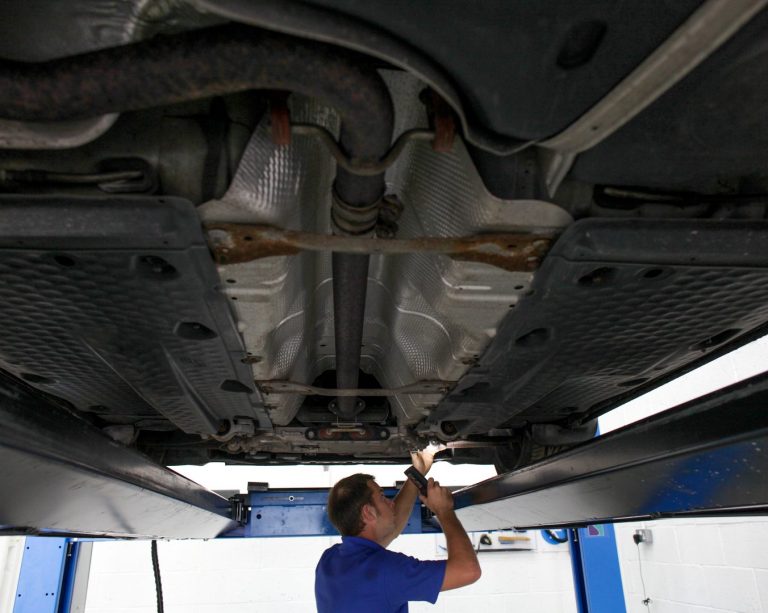 A vehicle technician examining the underside of a car during an MOT check