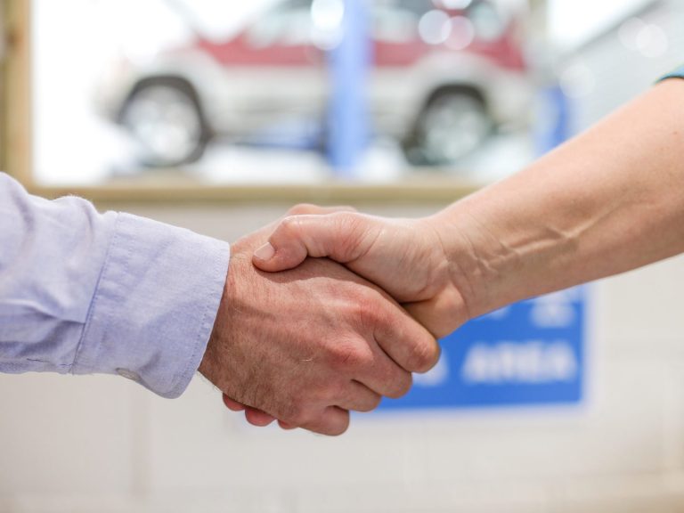 A friendly team member shakes hands with a happy customer at Phipps Motors