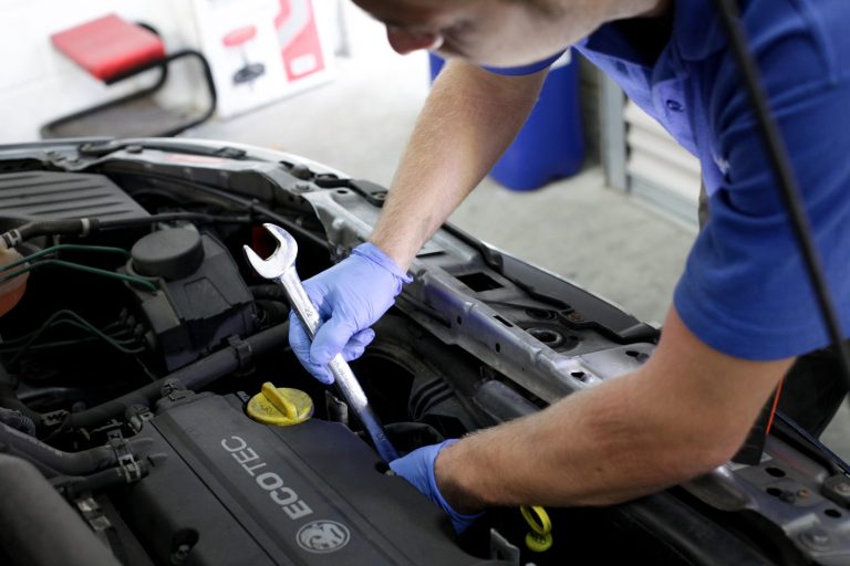 Our Services - Repairs A vehicle technician holding a spanner and working under the hood of a car