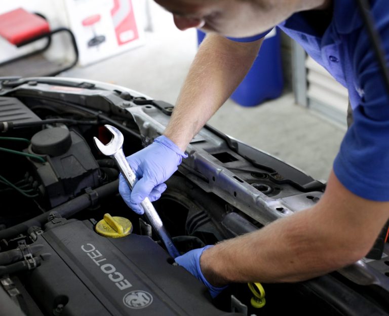 A vehicle technician holding a spanner, working underneath the hood of a car at Phipps Motors